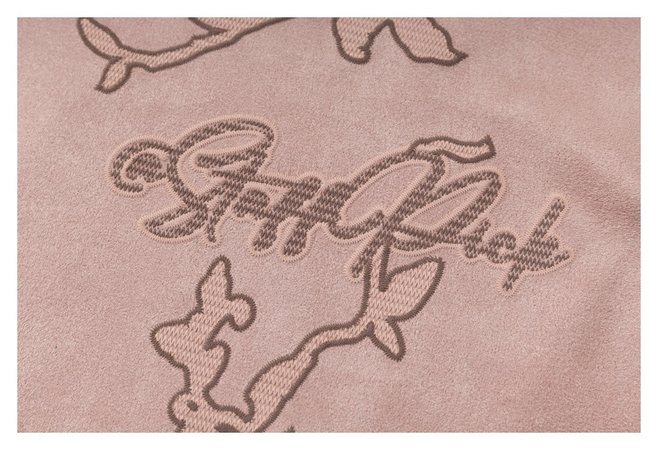 Close-up of decorative embroidered script and floral vine stitching on dusty pink fabric.