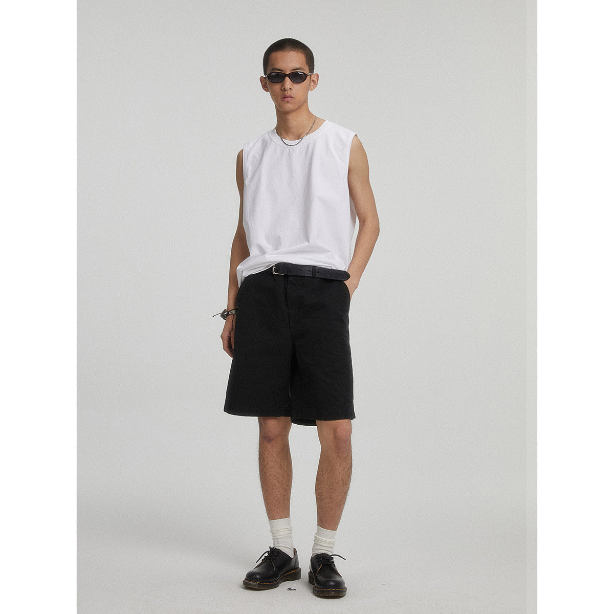 Model wearing a white sleeveless shirt and black knee-length shorts with a belt.
