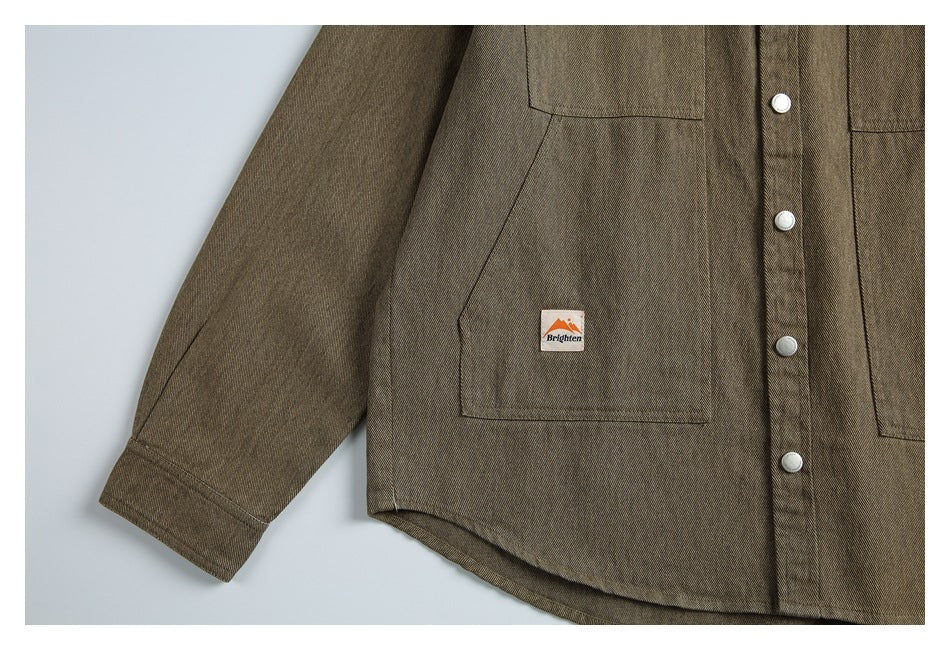 Close view of the brown-olive jacket's lower front, sleeve cuff, button placket, and small branded pocket patch.
