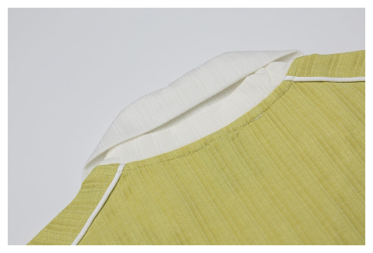 Close-up of a mustard-yellow textured garment with an ivory folded collar and narrow white piping.