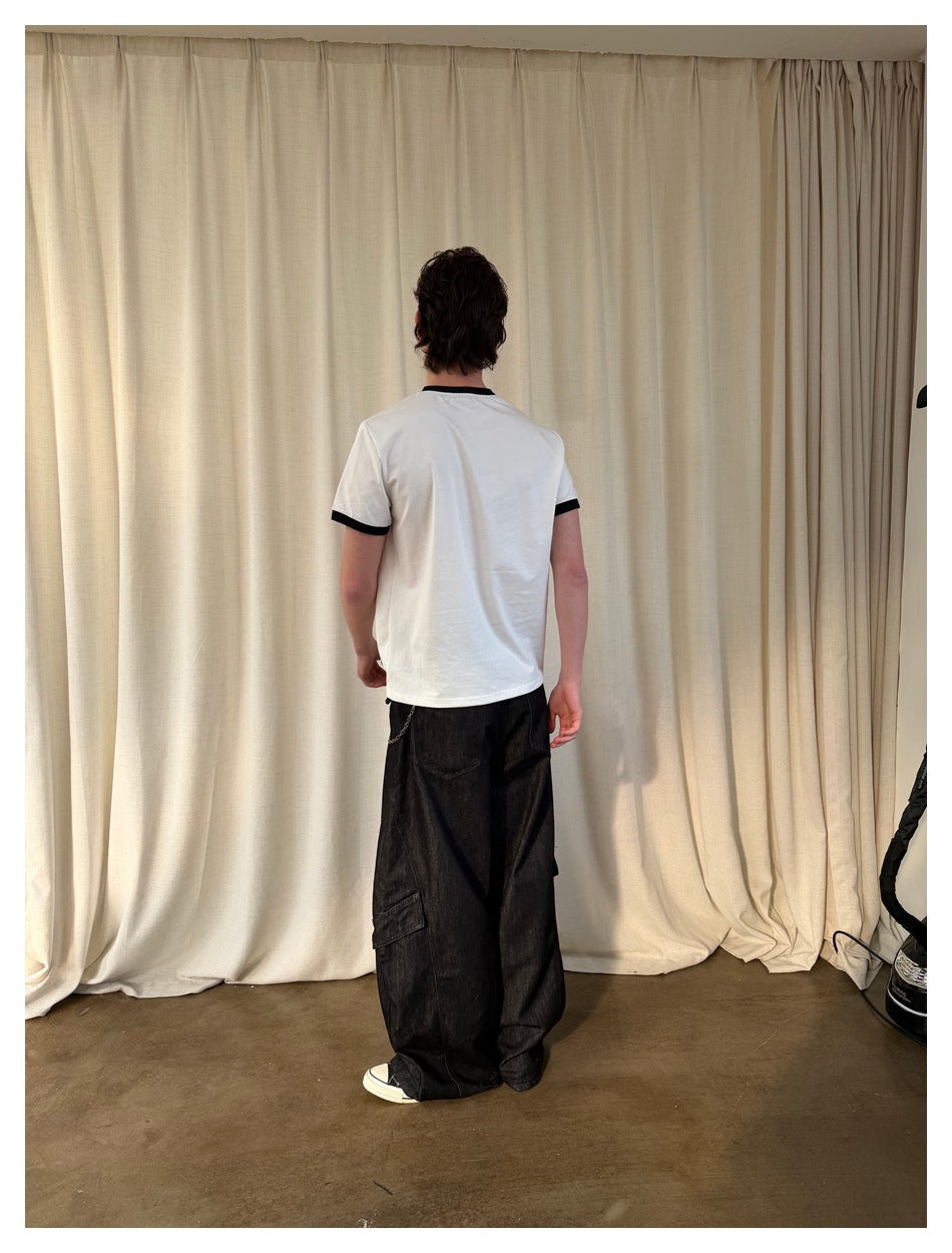 Back view of a model wearing a white T-shirt with black collar and sleeve trim, with wide dark cargo jeans