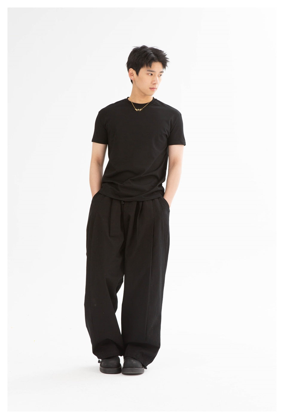 Man in a black short-sleeve crew-neck T-shirt and wide black trousers, turned slightly to the side