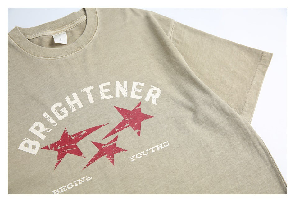 Close view of a sand-beige T-shirt front with distressed white lettering and three red stars.