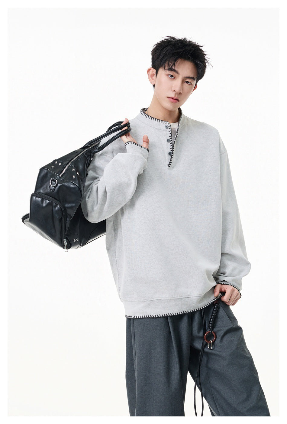 Model wearing a light gray oversized pullover with black contrast stitching and a short button placket.