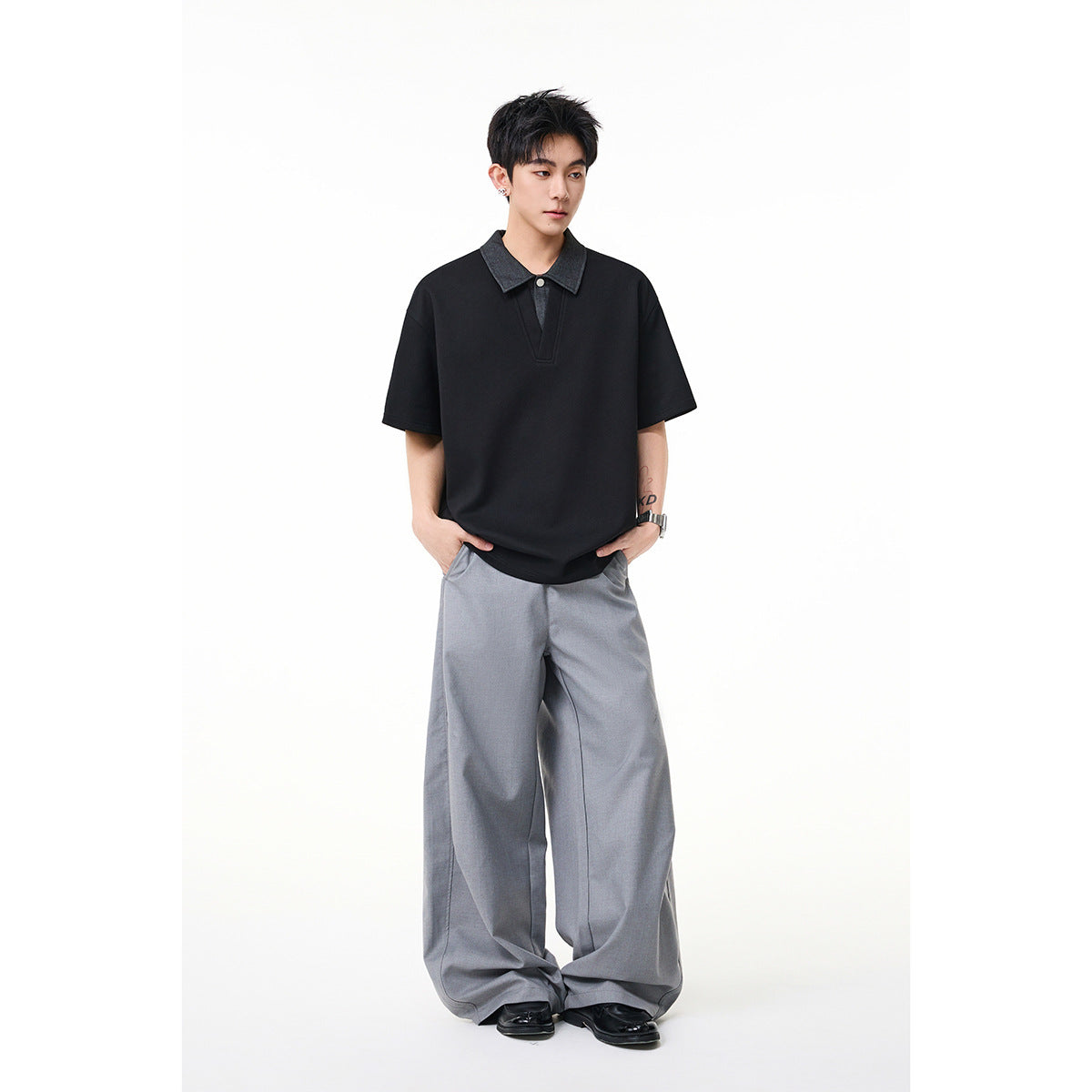 Model wearing a black short-sleeve polo-style shirt with a dark gray collar and loose light gray trousers.