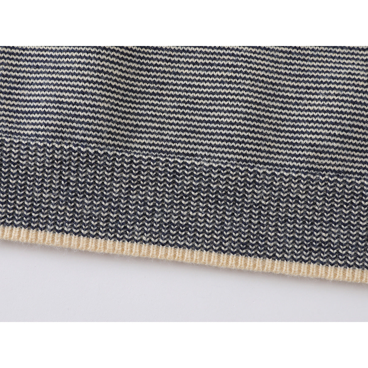Close-up of the sweater hem, showing navy and cream knit stripes and a cream ribbed edge.
