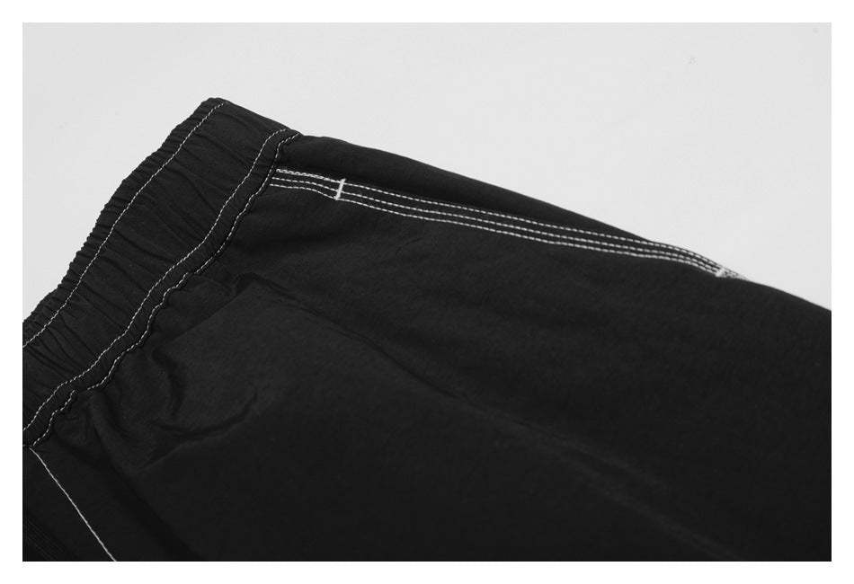 Close-up of the black pants' waistband, pocket area, and parallel rows of light contrast stitching.