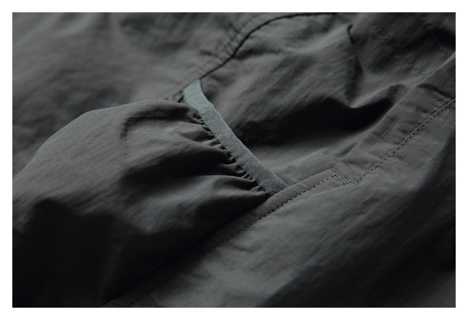Close-up of a dark charcoal garment's pocket opening, gathered edge, and stitching.