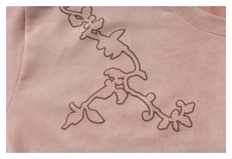 Close-up of dusty pink fabric with dark outlined floral vine embroidery.