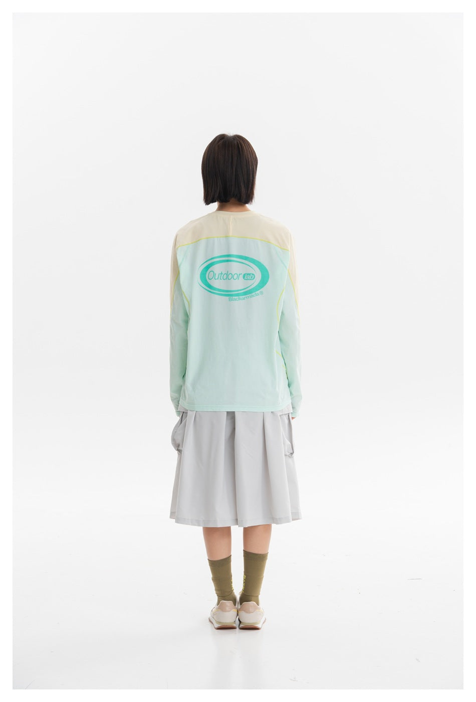 Rear view of a woman wearing a pale mint shirt with cream shoulders and sleeves; an oval graphic is printed on the back.