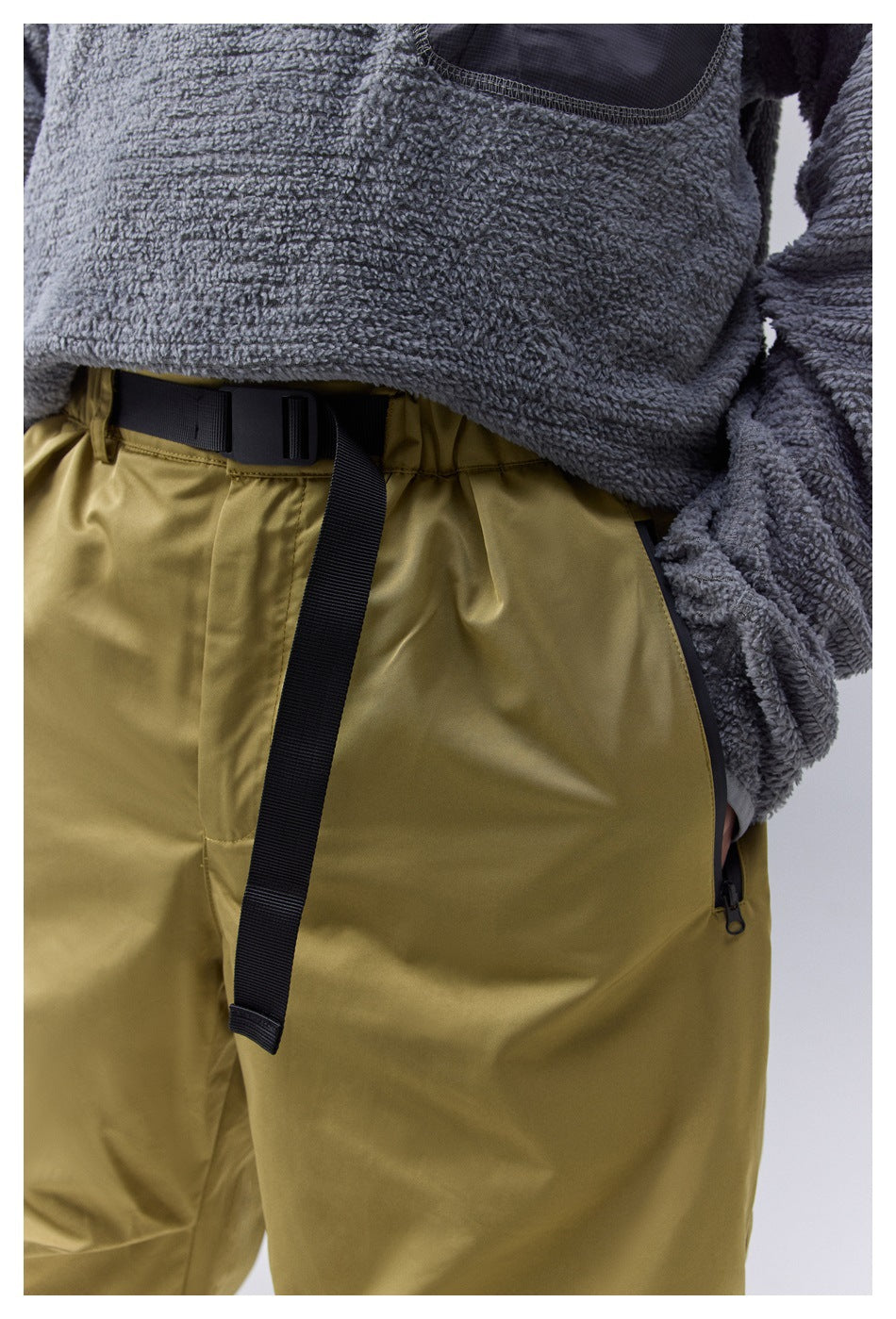 Close-up of olive-yellow pants showing a black waist belt and side pocket zipper.