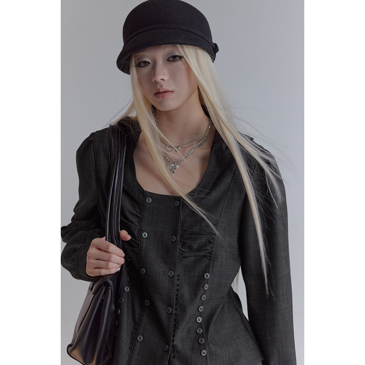 Close view of a model wearing a charcoal blouse with a square neckline, puff sleeves and rows of buttons.