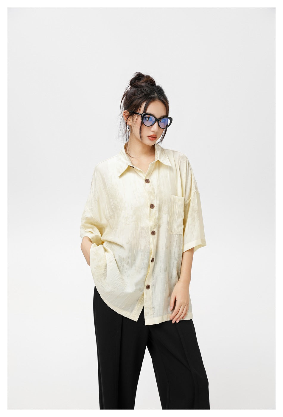 Model wearing a loose ivory patterned short-sleeve button-up shirt with a chest pocket and black trousers.