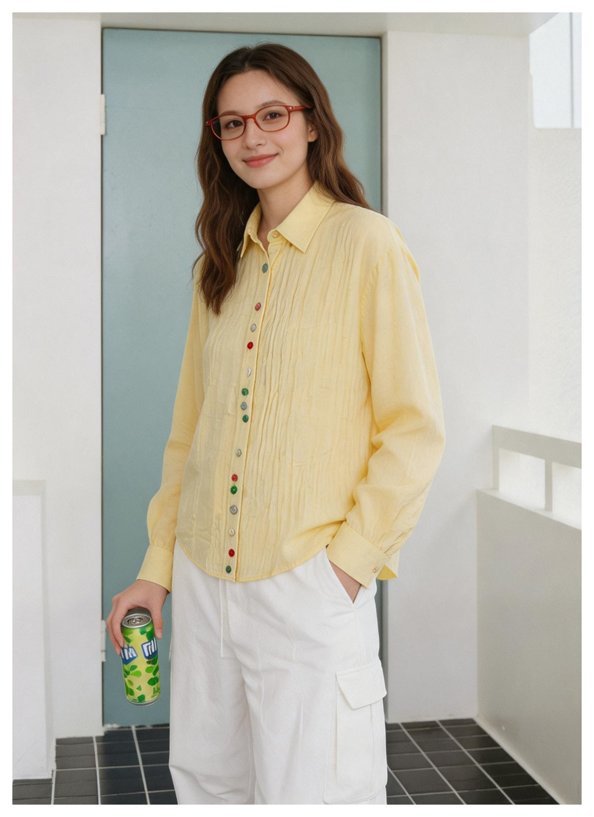 Woman wearing a pale yellow button-up shirt with multicolor buttons and white cargo pants, holding a beverage can