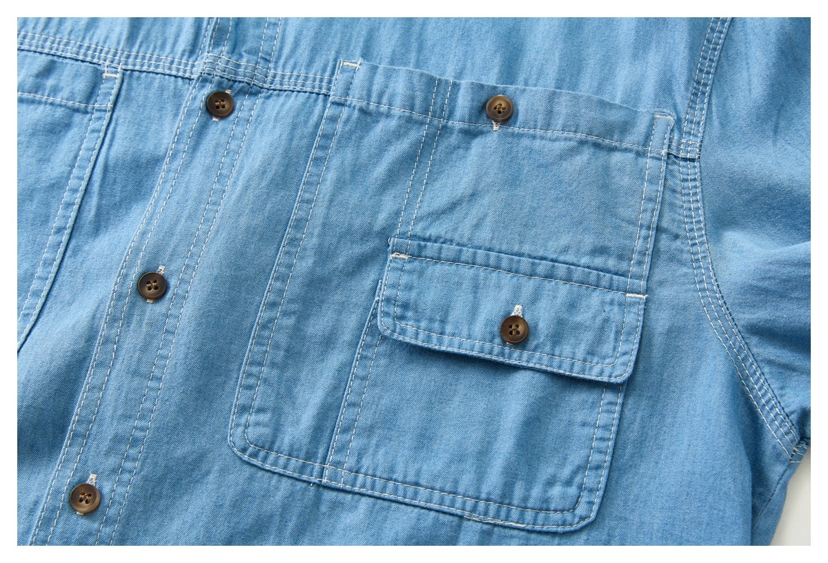 Close-up of a light blue shirt's chest pocket with button flap, brown buttons, and contrast stitching.