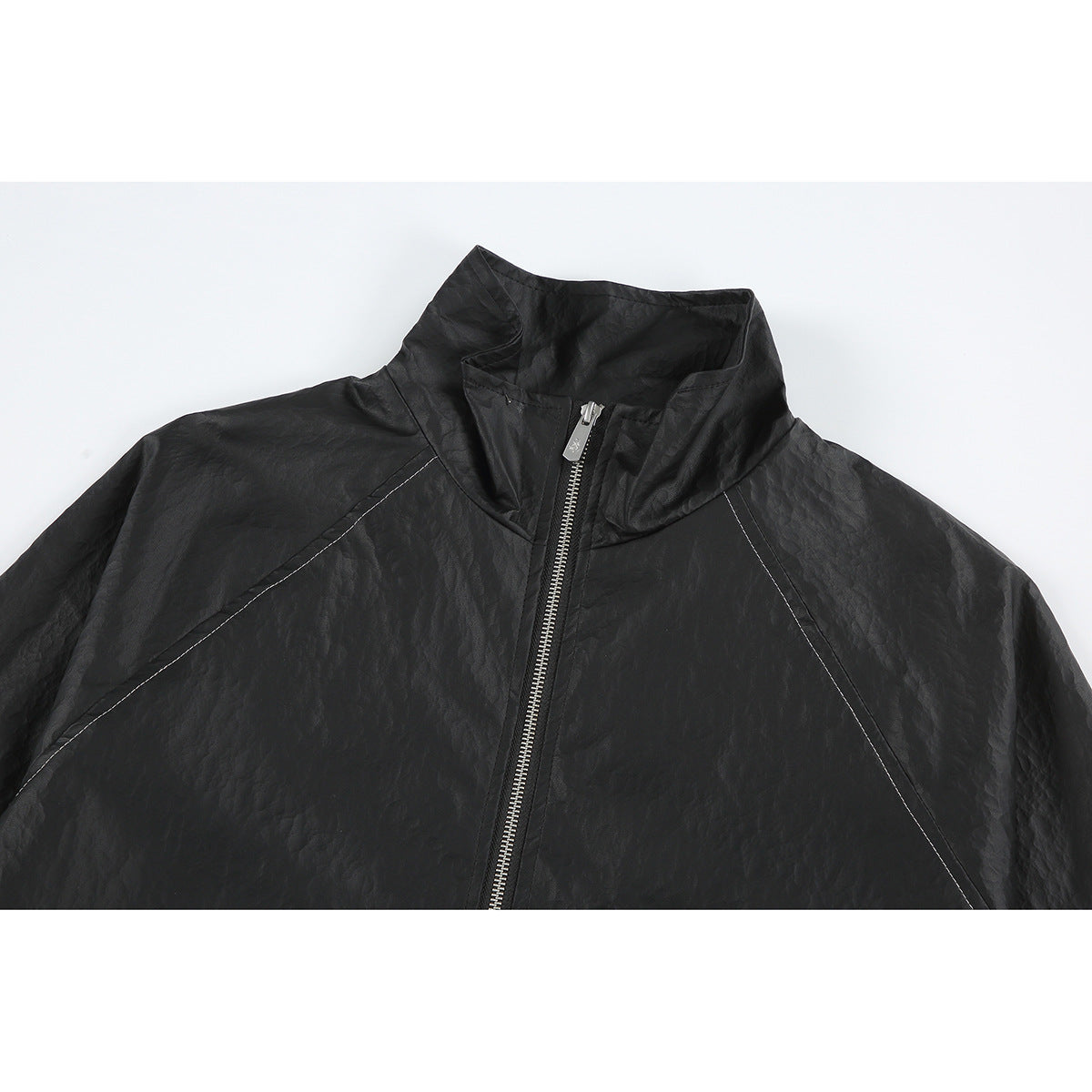 Close-up of a black jacket’s stand collar, silver front zipper, and contrast raglan seam stitching.