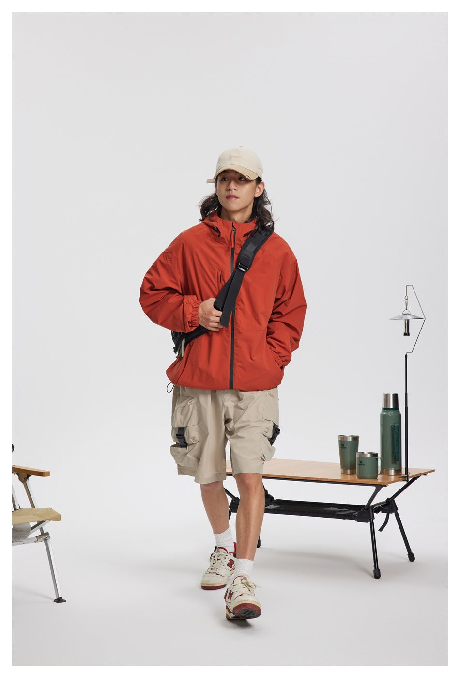 Full-length view of a person wearing a rust-red hooded jacket, beige cargo shorts, and a crossbody bag.