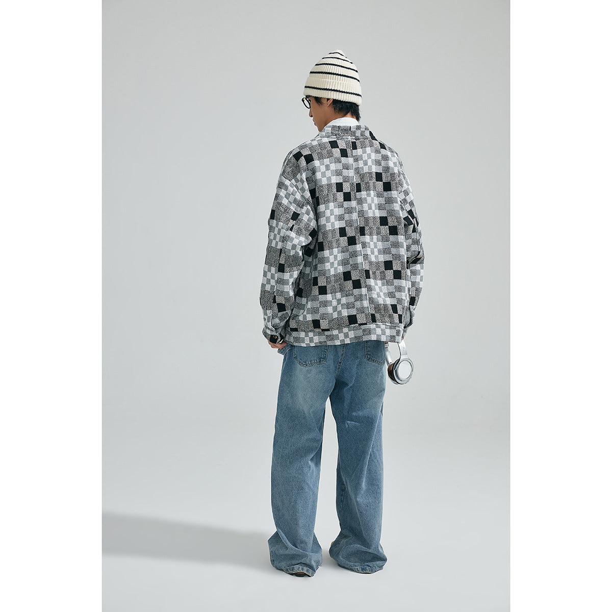 Rear view of a model wearing a black, gray and white patchwork-check cardigan with blue jeans.