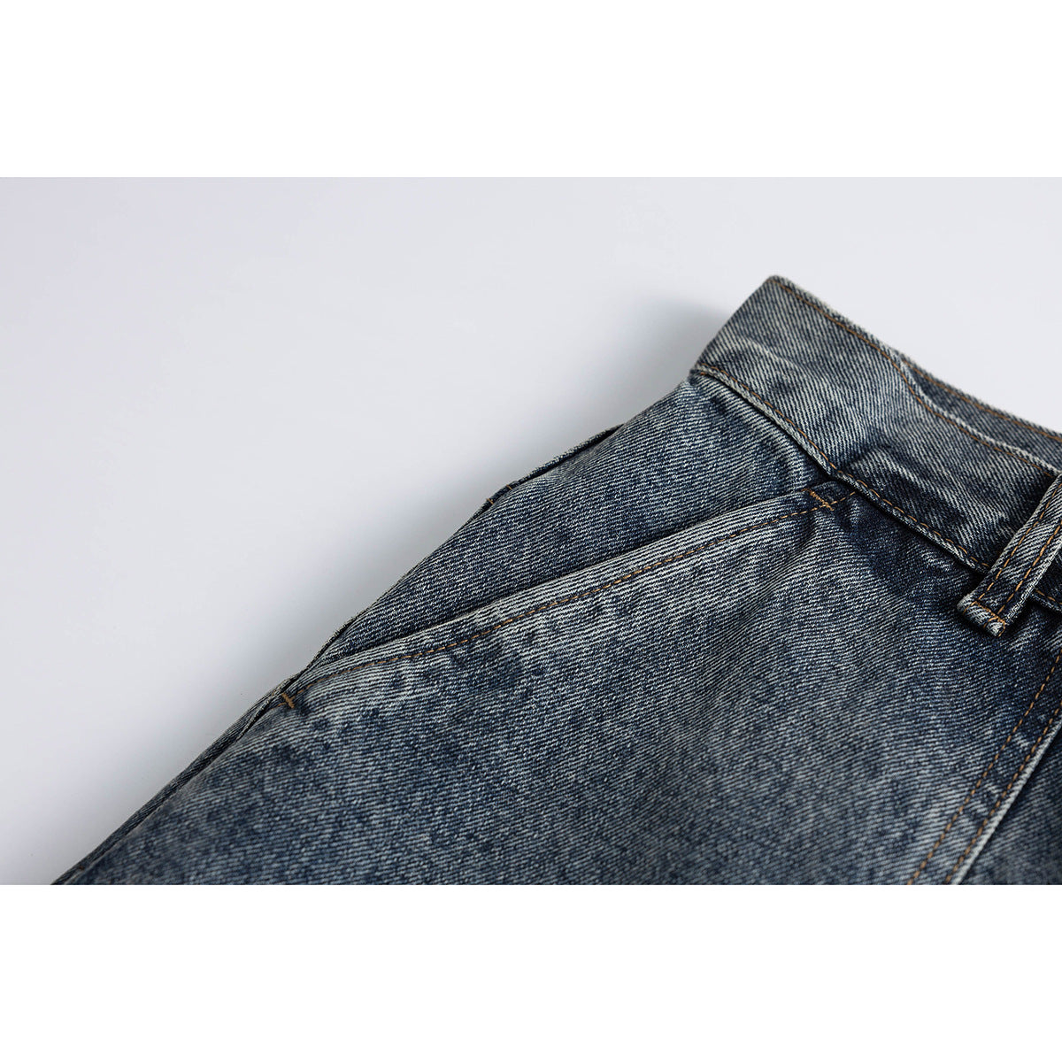 Close-up of washed blue-gray jeans showing a slanted front pocket and waistband with a belt loop.