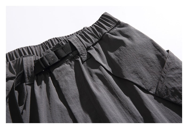 Close-up of the charcoal shorts' elastic waistband, black buckle belt, and large side pocket.
