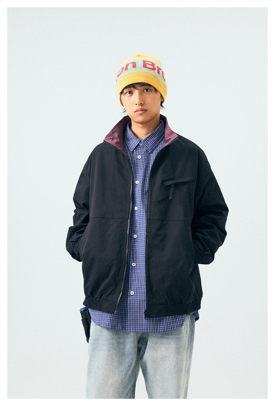 Front view of a model wearing a black zip-front jacket with plum collar lining and a blue checked shirt.