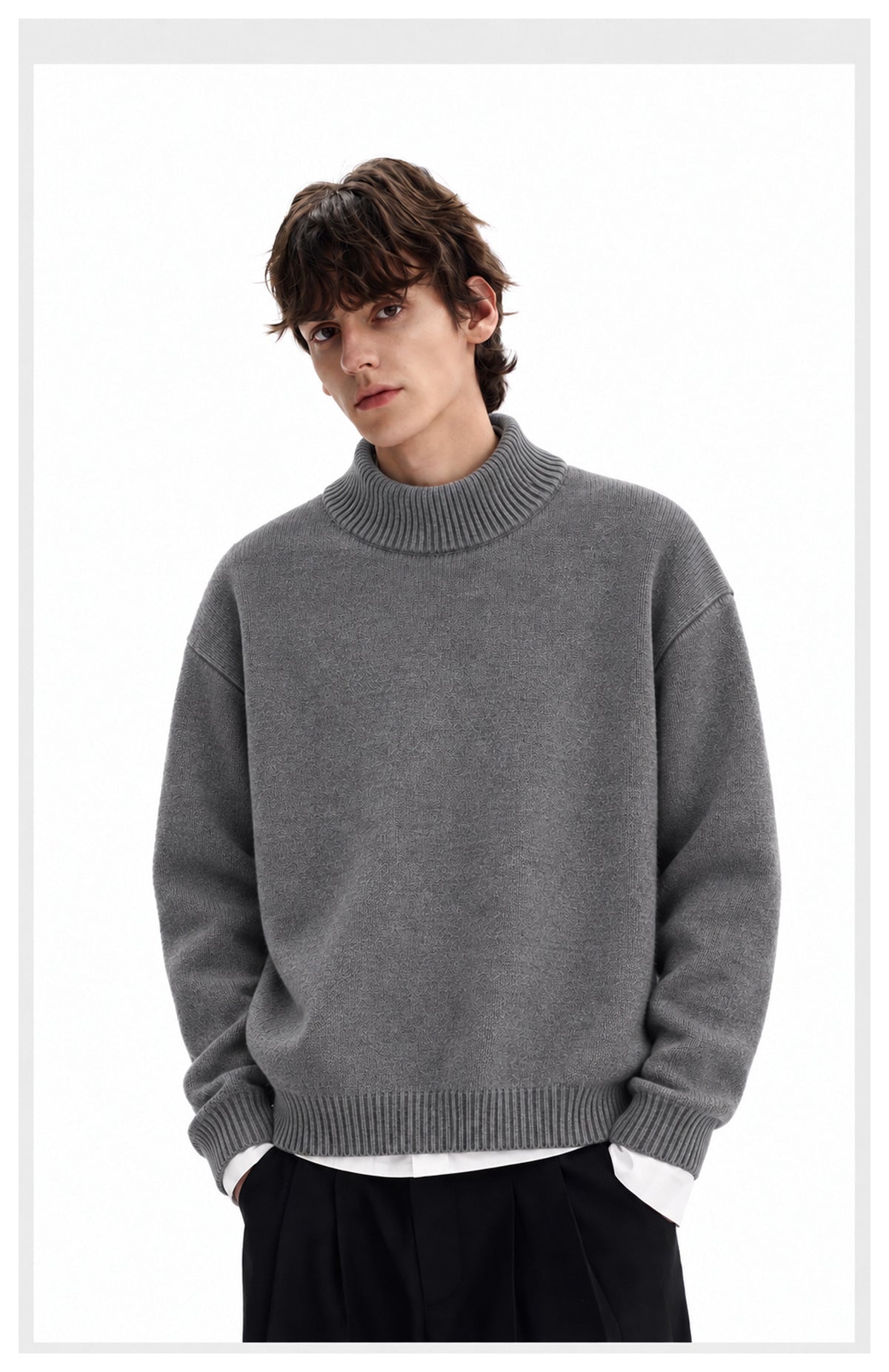 Man models a textured gray high-neck sweater with ribbed trim over a white shirt and black trousers.