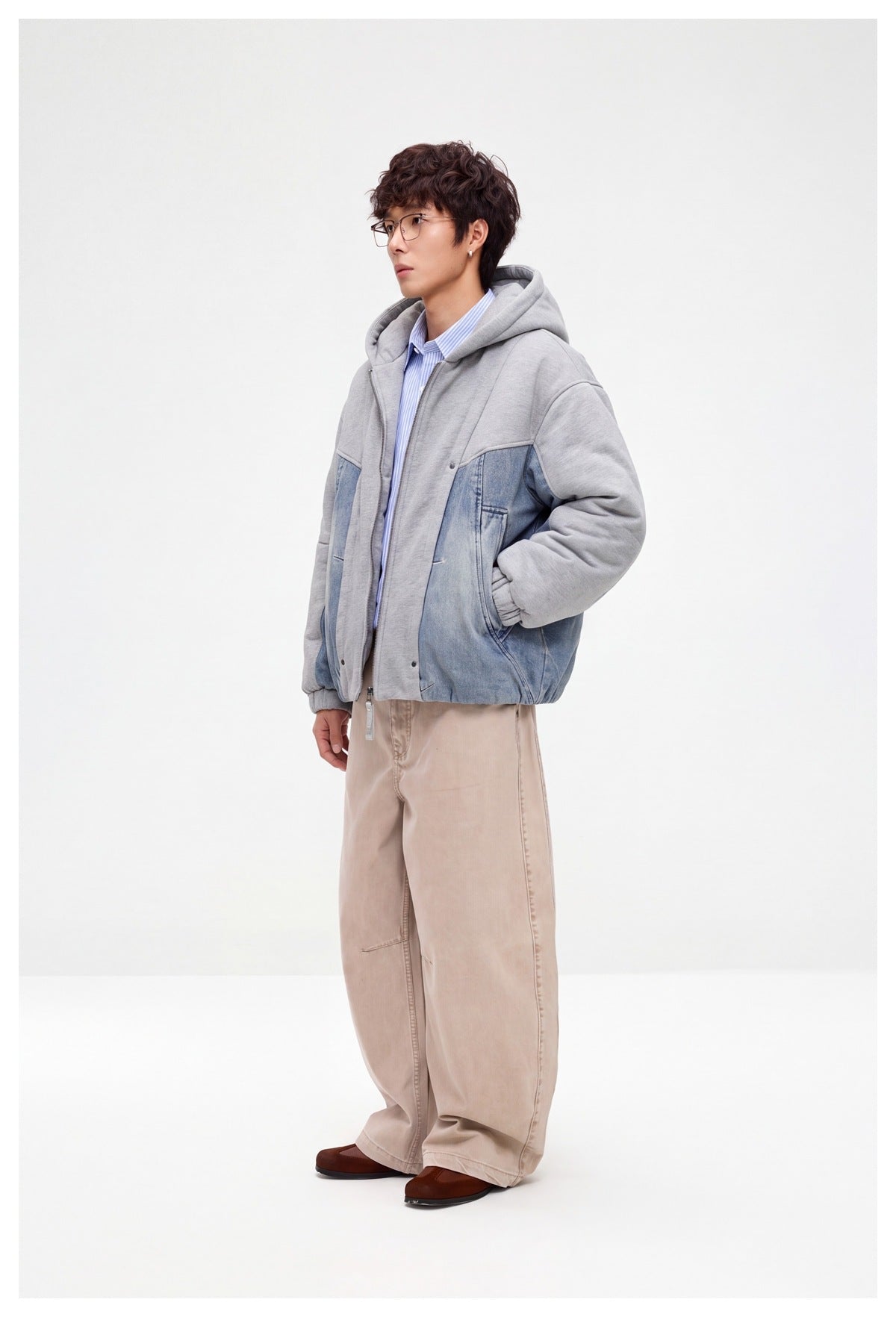 Side view of a model wearing a gray hooded jacket with blue denim panels and loose beige trousers.