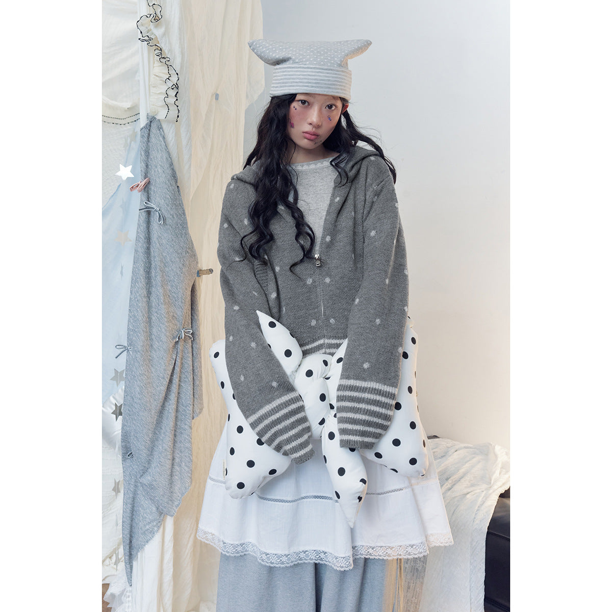 Model wearing a gray spotted zip hoodie with striped cuffs, a white skirt and polka-dot pillows.