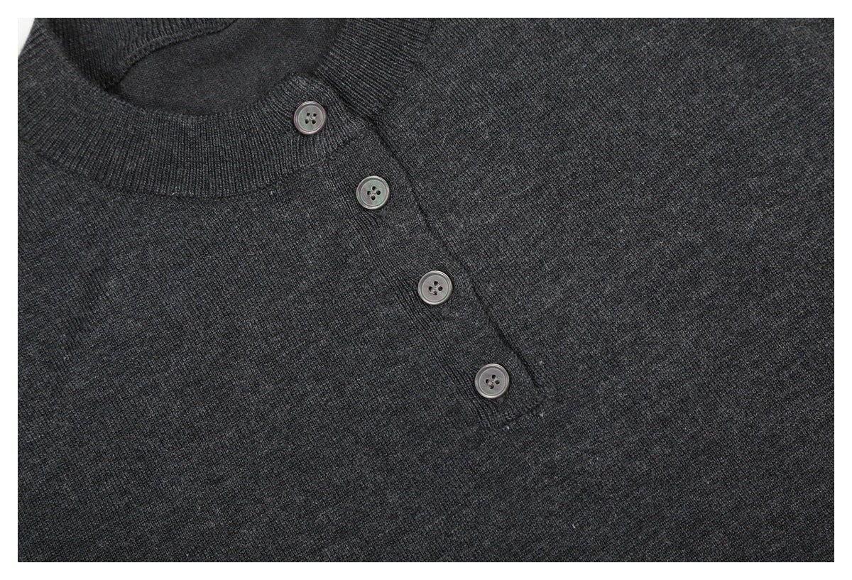 Close-up of four buttons on the angled placket of a charcoal knit top.