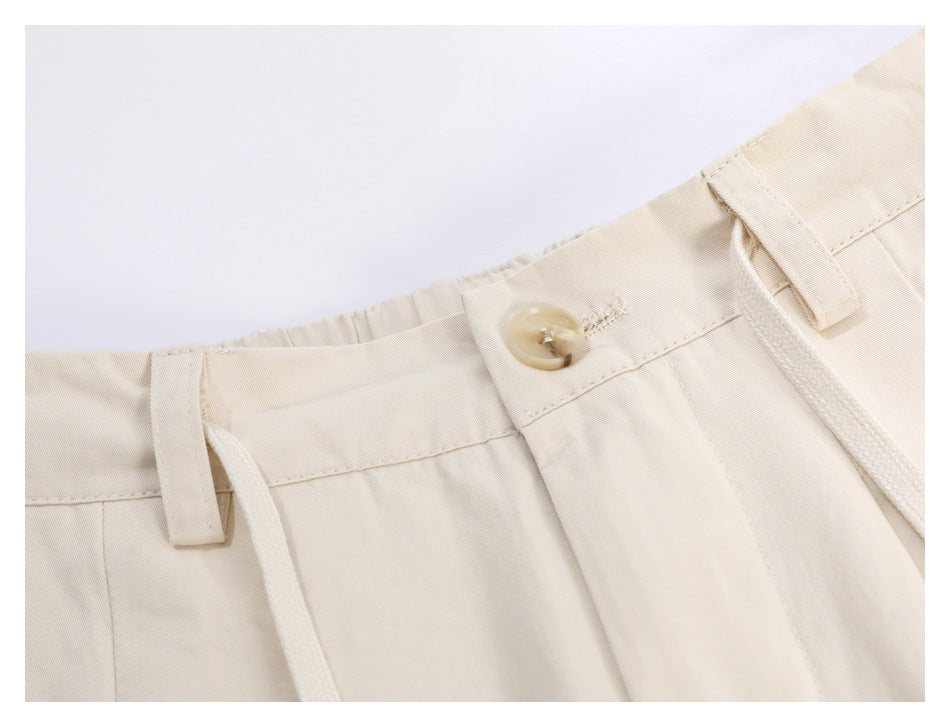 Close-up of ivory trousers showing the waistband button, belt loop, drawstring and front pleats.