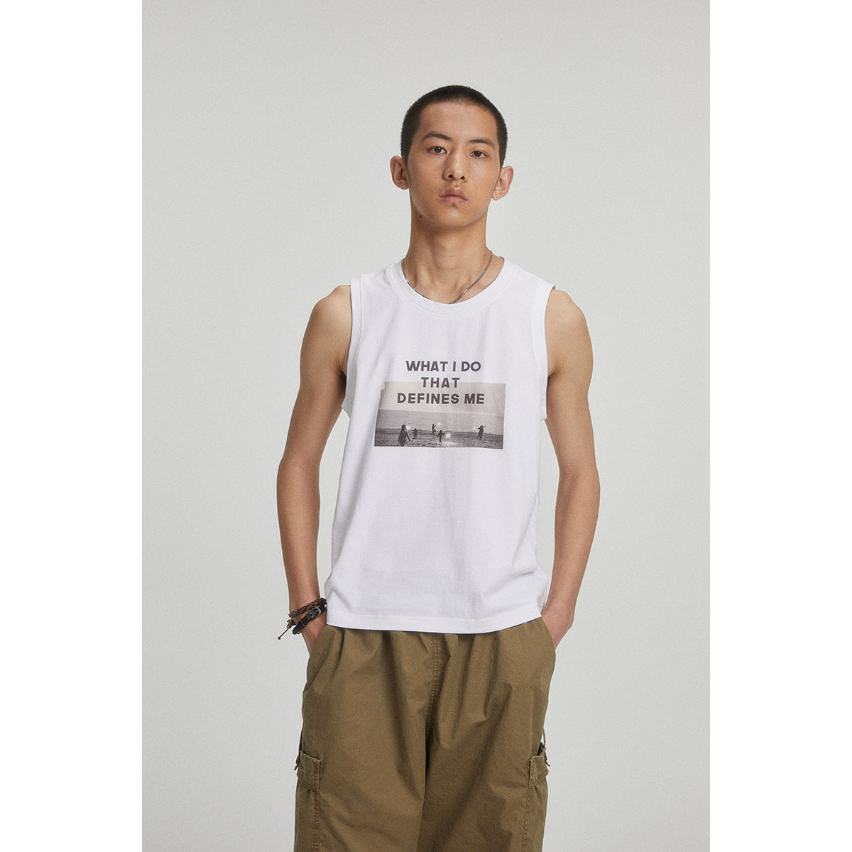 Model wearing a white sleeveless shirt with text and a beach photo graphic, paired with olive cargo pants.