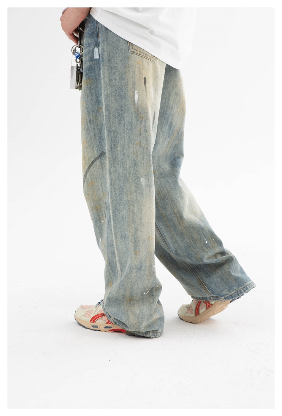 Angled side view of wide faded blue jeans with distressed marks, worn with a white shirt.