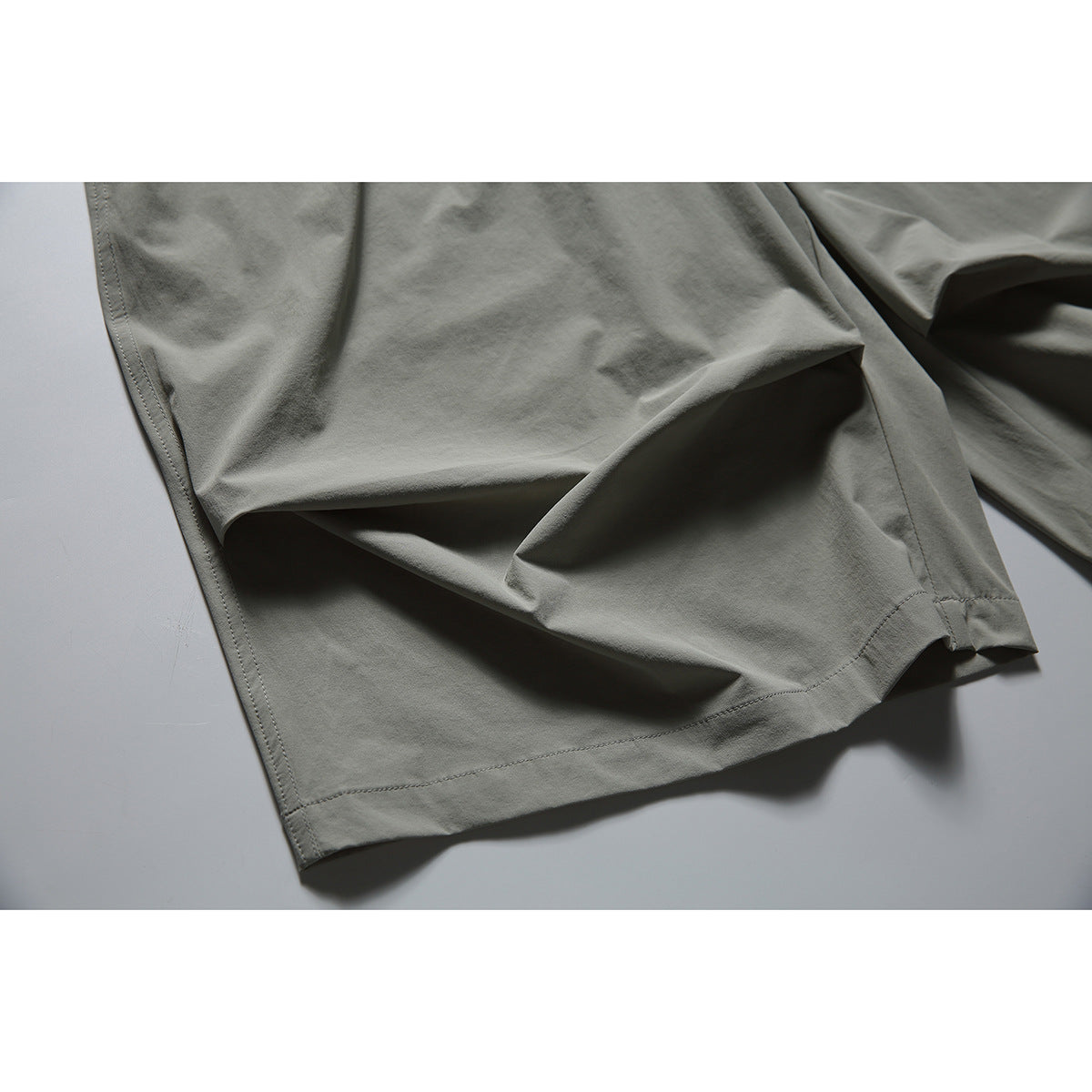 Close-up of the gray-green shorts' wide leg opening and stitched hem.