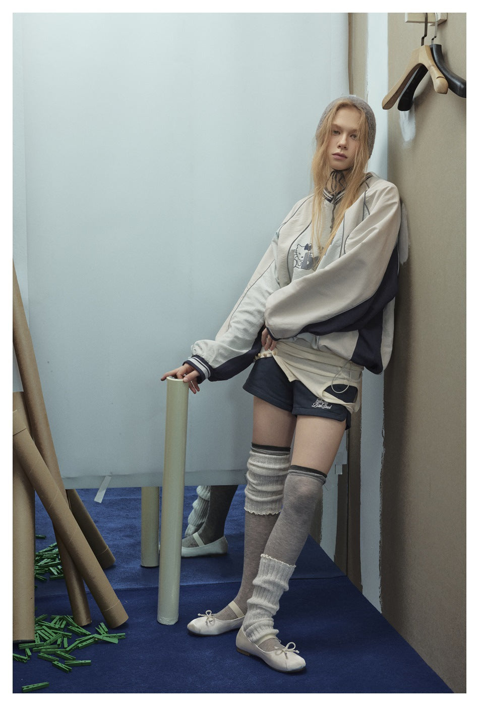 Model leaning on a wall in a light gray pullover with navy side panels, striped cuffs and drawcord hem
