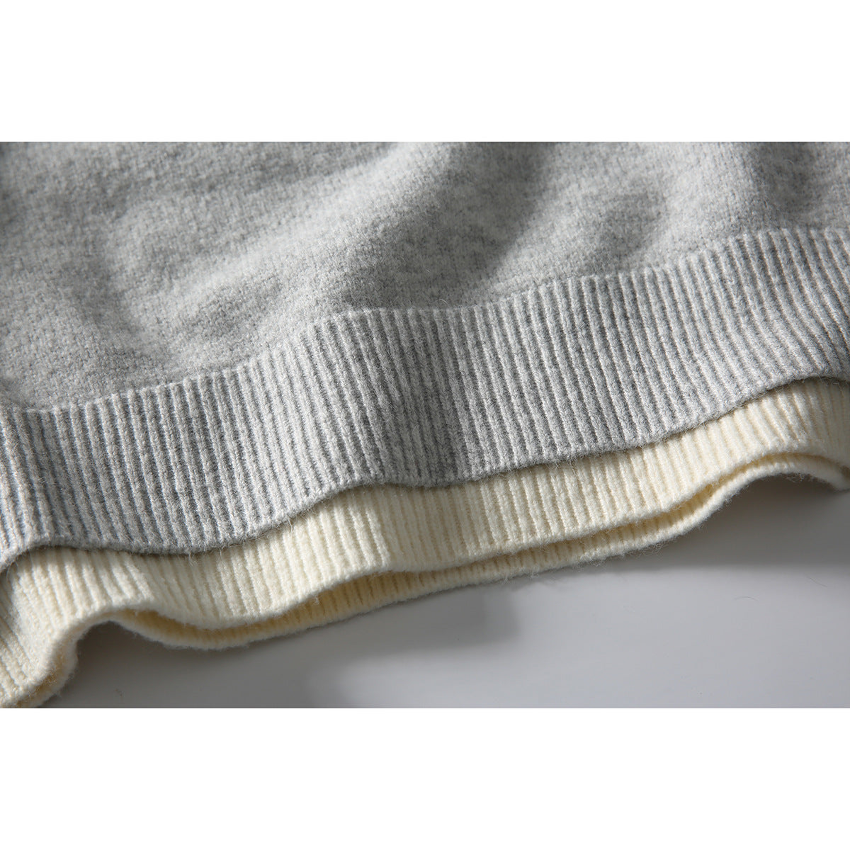 Close-up of layered gray and cream sweater hems with ribbed edging.