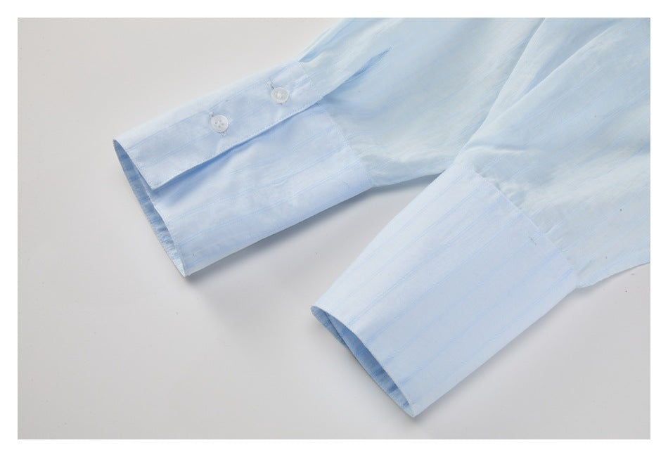 Close-up of the pale blue striped shirt's long sleeves, showing wide buttoned cuffs.