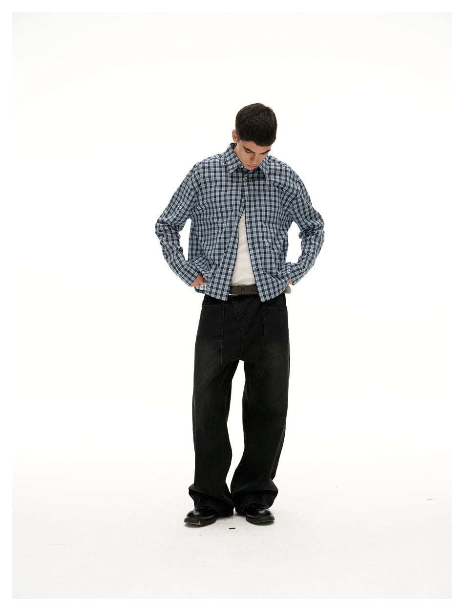 Model wearing a blue, gray, and black plaid button-up shirt over a white tank with wide black trousers.