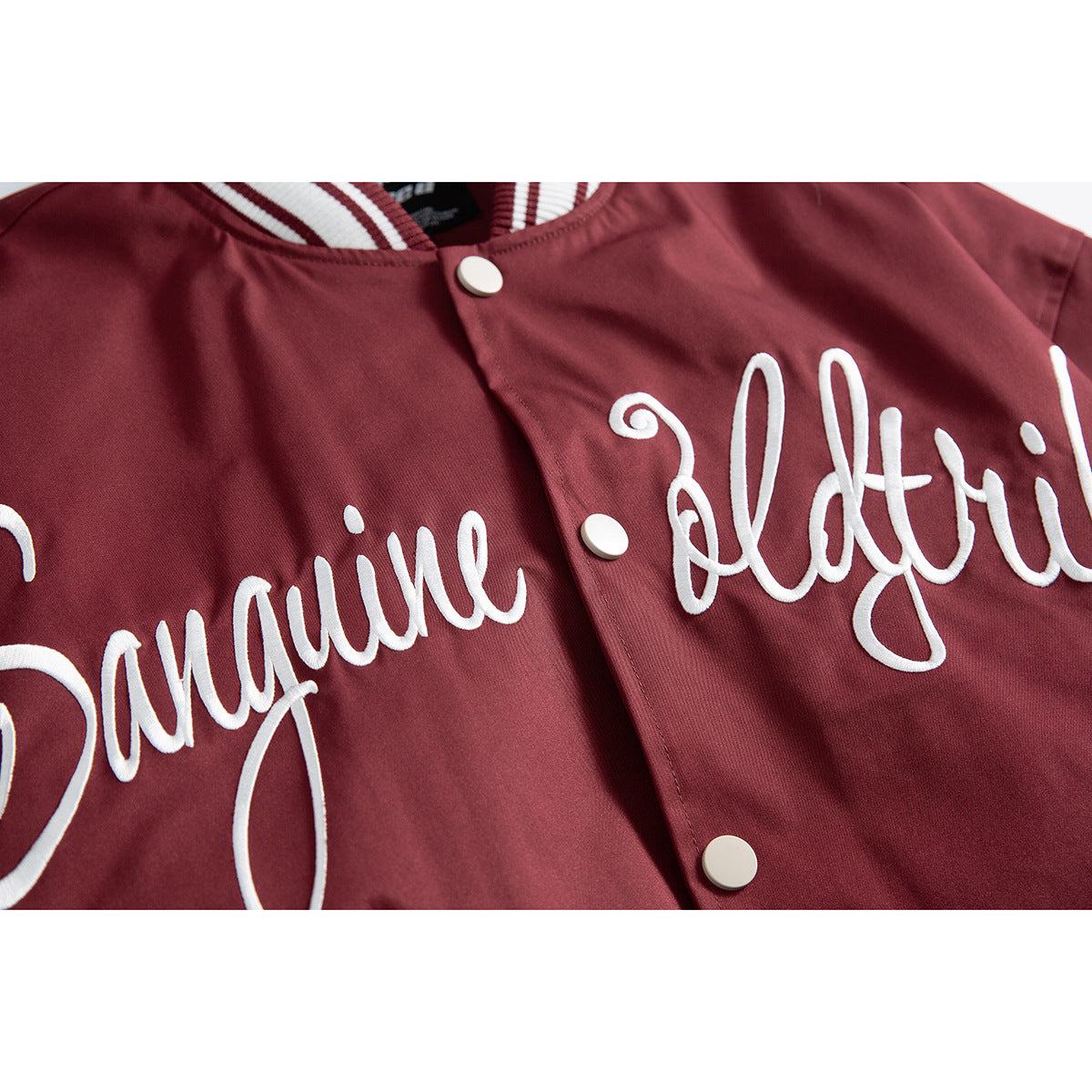 Close-up of white cursive lettering and snap buttons on the burgundy jacket front.