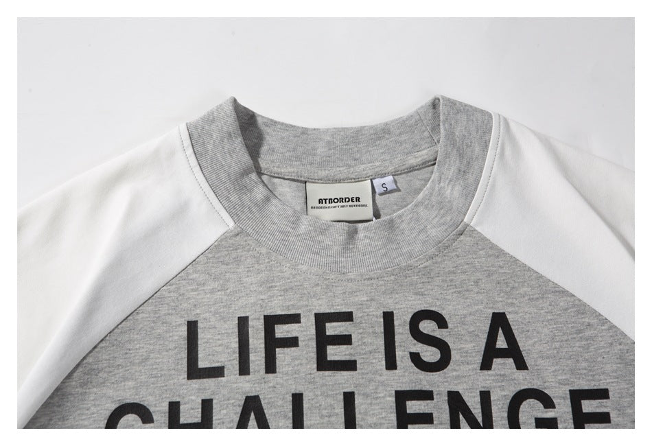 Close-up of the sweatshirt’s gray ribbed neckline, neck label, white raglan sleeves, and black lettering.