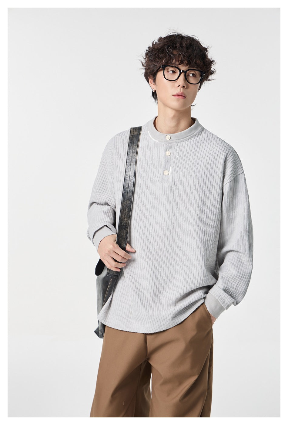 Model wearing a pale gray textured three-button top and brown trousers, with a black shoulder bag.