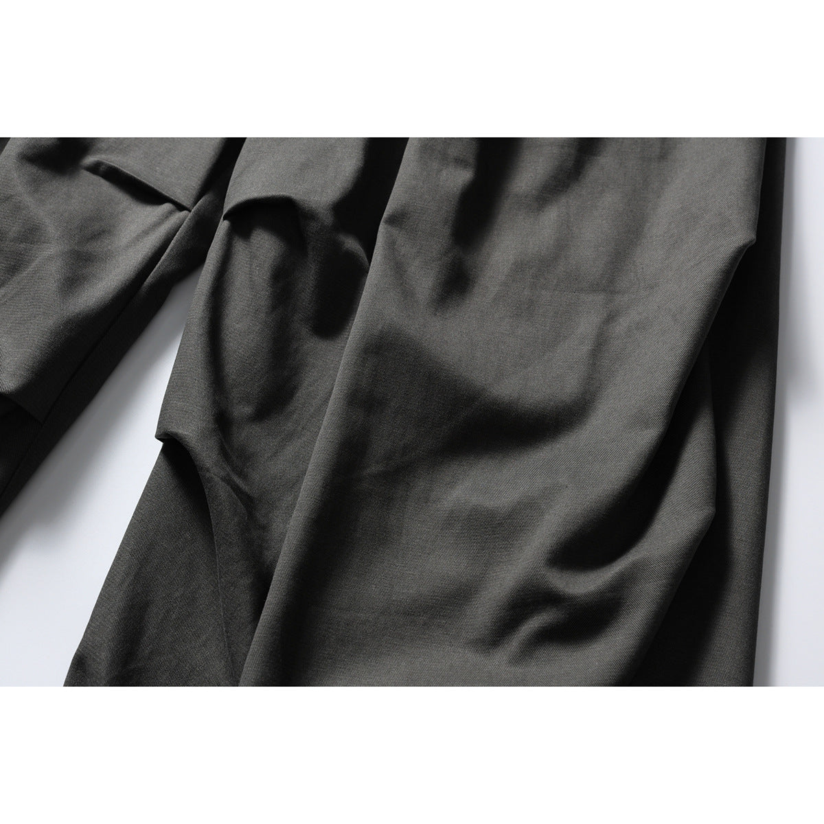 Close-up of dark charcoal trousers showing the draped fabric and folds.
