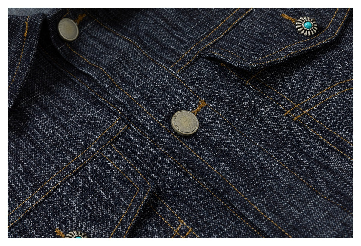Close-up of dark indigo denim with golden-brown stitching, metal buttons, and turquoise ornamental accents.