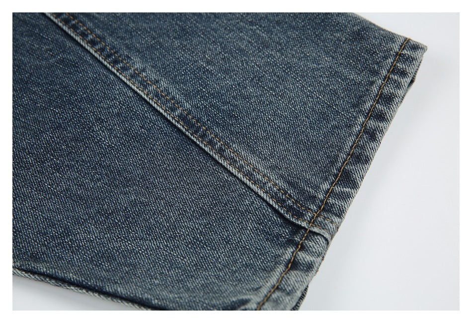 Close-up of blue denim jeans showing a folded edge and parallel tan stitching.
