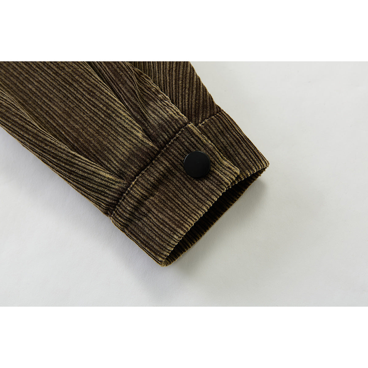 Close-up of the brown corduroy jacket sleeve cuff with a black snap button.