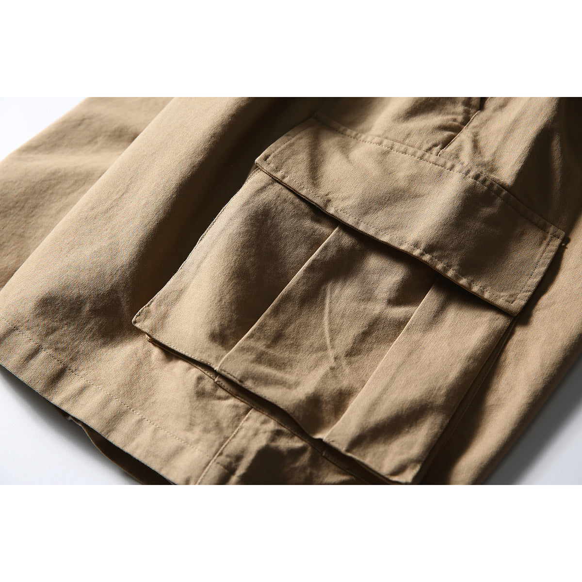 Close-up of tan cargo shorts showing a layered flap pocket and stitched seams.