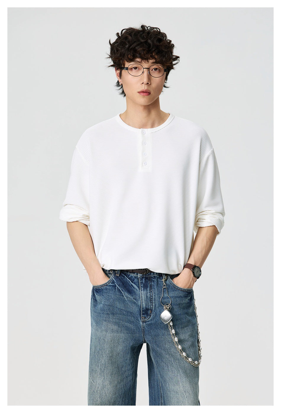 Man wearing a white ribbed long-sleeve Henley top with four buttons, with hands in the pockets of blue jeans