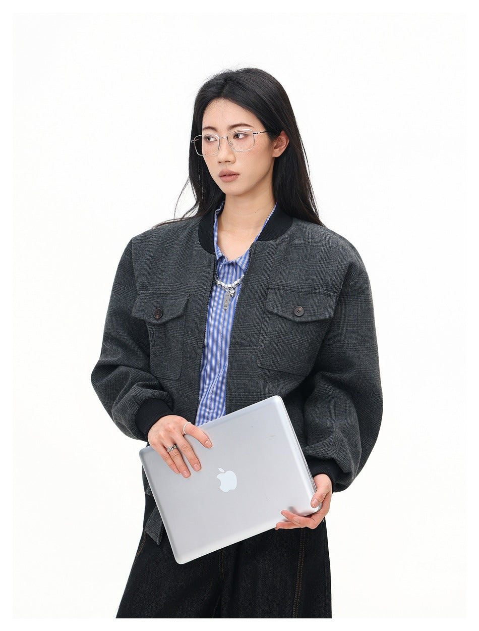 Model wearing an open charcoal plaid bomber jacket with black ribbed trim and button-flap chest pockets.