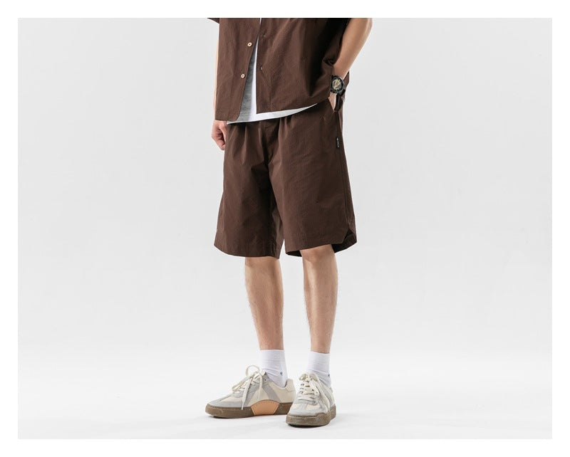 Front three-quarter view of a model wearing loose dark brown shorts with a matching top and white sneakers.