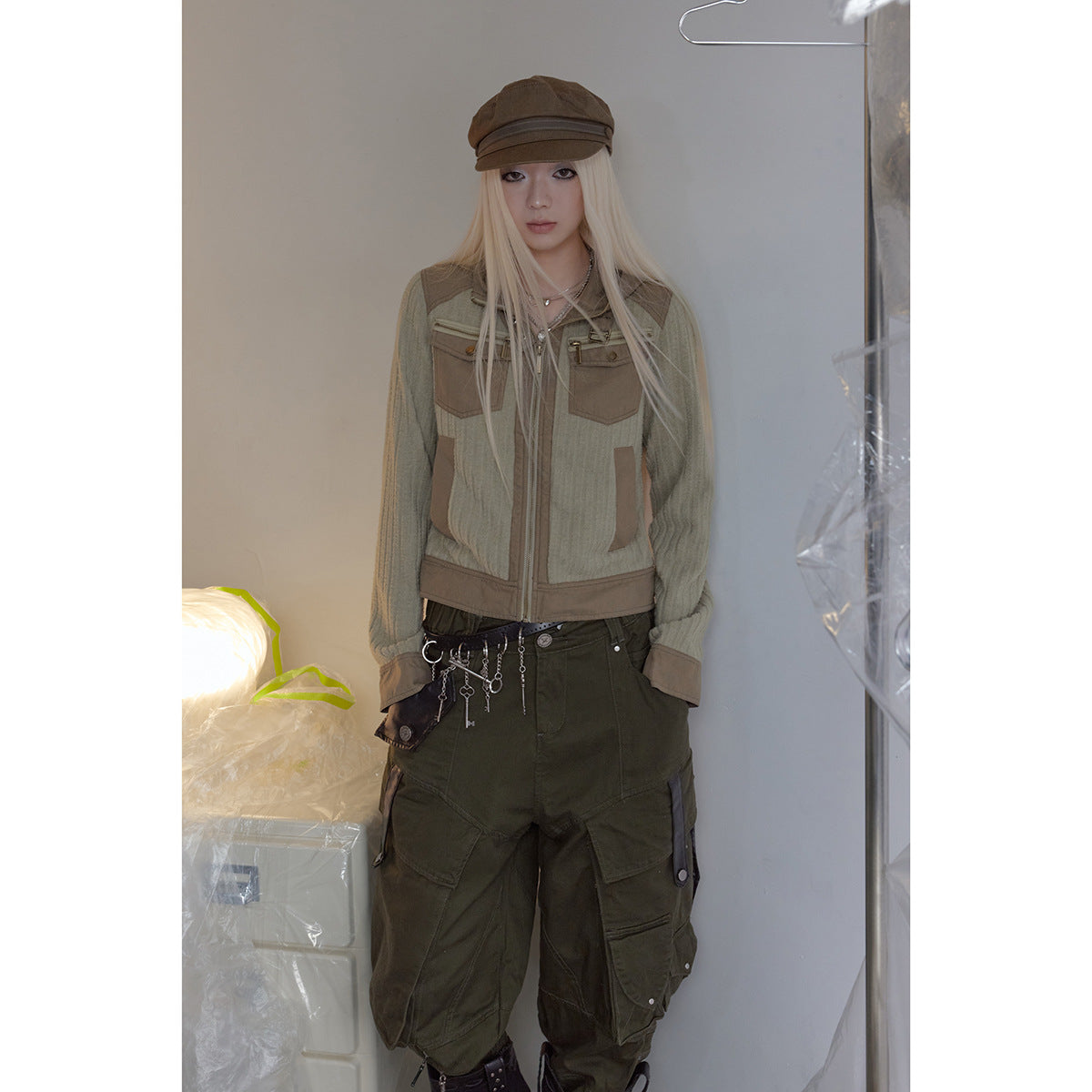 Front view of a model wearing a sage and tan zip jacket with dark olive cargo pants and a brown cap.