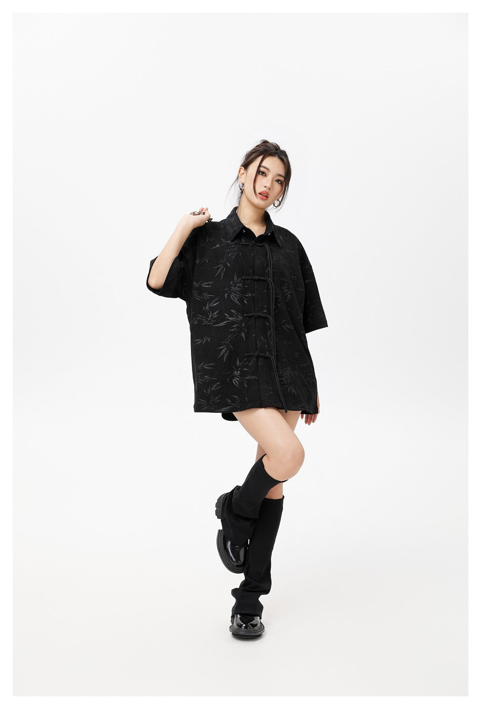 Model posing in an oversized black short-sleeve shirt with a subtle leaf pattern and knotted closures.